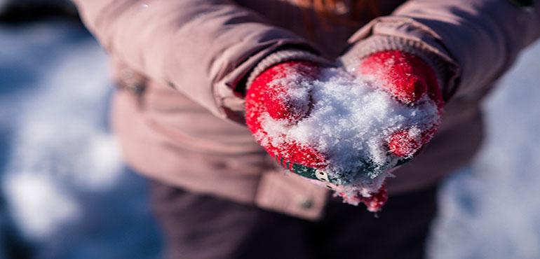 A person in a pink coat and red mittens holding a snowball. (Image by Dmitriy Gutarev from Pixabay)